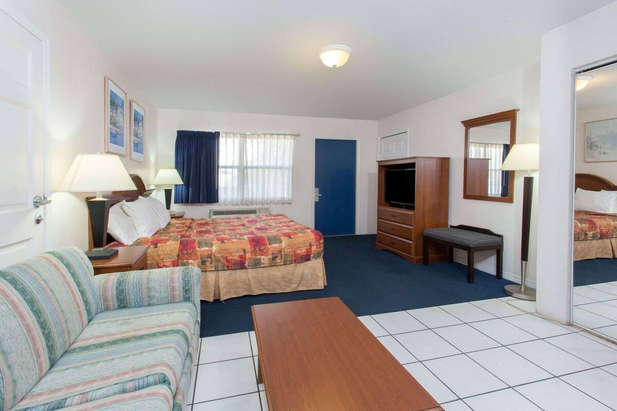 Una habitación de hotel con cama, sofá, escritorio, televisor y espejo.