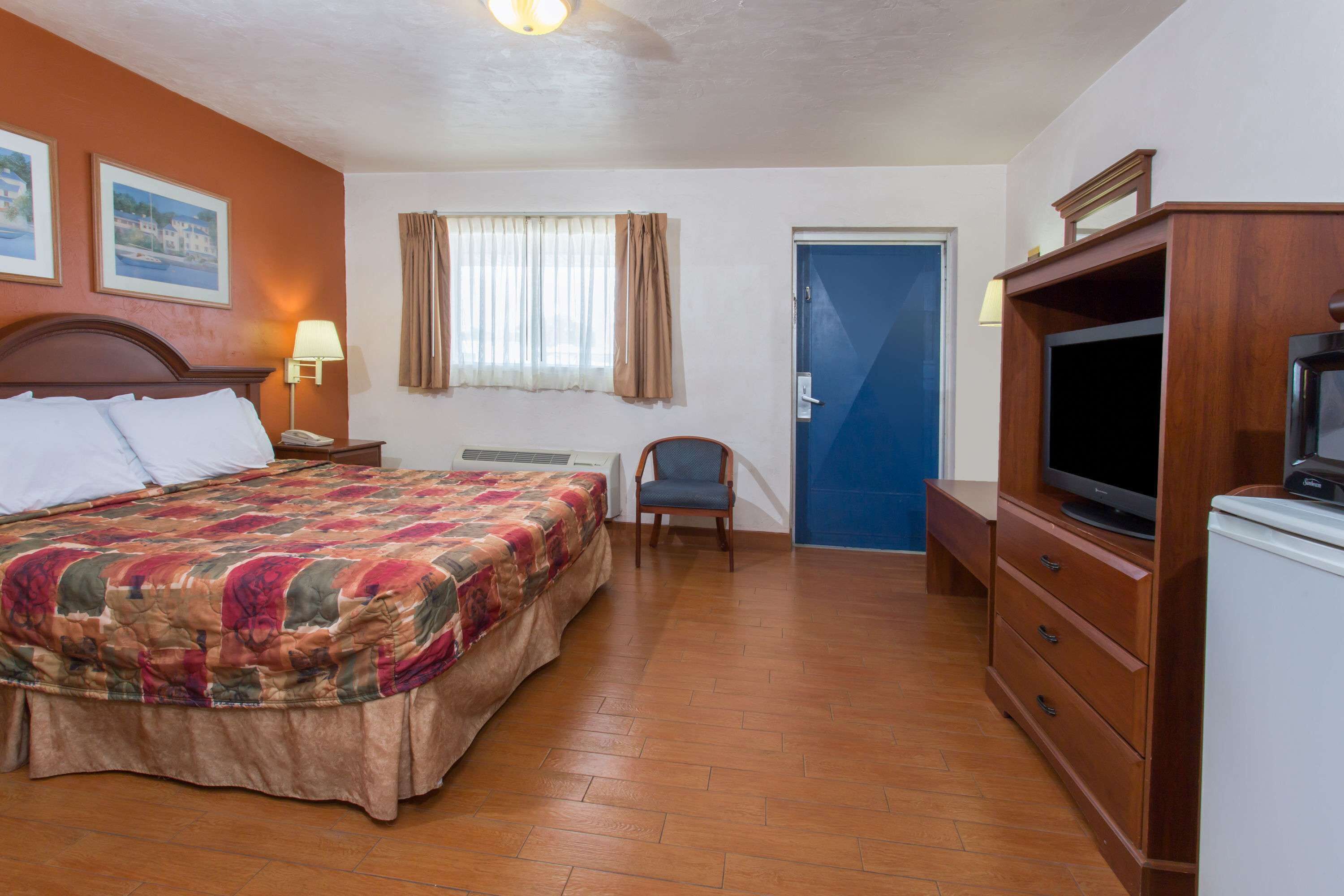 A hotel room with a bed, a chair, a TV, and a dresser.