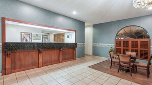 A reception area with a wooden counter, tiled floor, and a dining area with chairs and a table. - Knights Inn Arcadia (Arcadia)