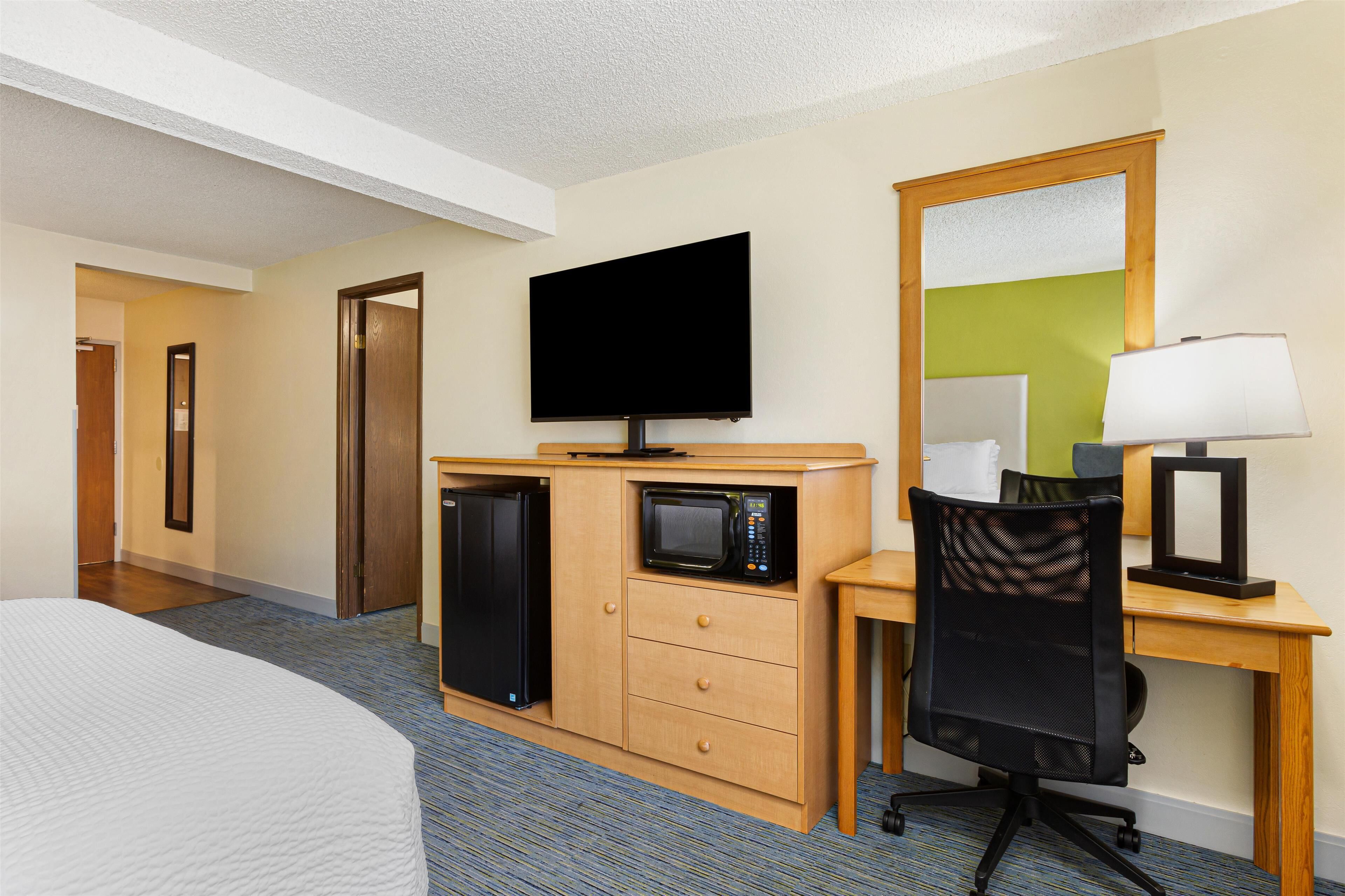 A hotel room with a bed, a desk with a computer, a television, a microwave, and a refrigerator.