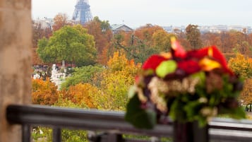 Une vue sur la Tour Eiffel depuis un balcon, avec le feuillage automnal en arrière-plan, un vase rempli de fleurs et un bureau avec un carnet et un stylo.