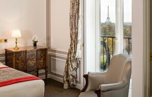 A hotel room with a bed, a chair, a lamp, and a view of the Eiffel Tower. - Hotel Regina Louvre (Paris)
