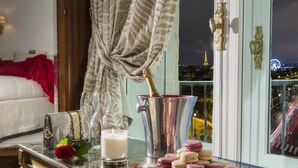 Una mesa con macarons, una vela y una botella de champán en una habitación con vista a la Torre Eiffel.