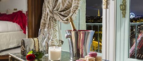 A table with macarons, a candle, and a bottle of champagne in a room with a view of the Eiffel Tower.