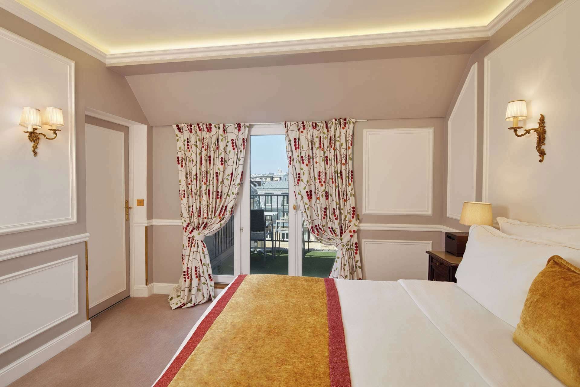 A hotel room with a bed, a window with curtains, a balcony, and wall sconces.
