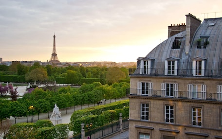 A view of the Eiffel Tower from a building with a sloped roof, a statue in the foreground, and a park with trees and a fountain.