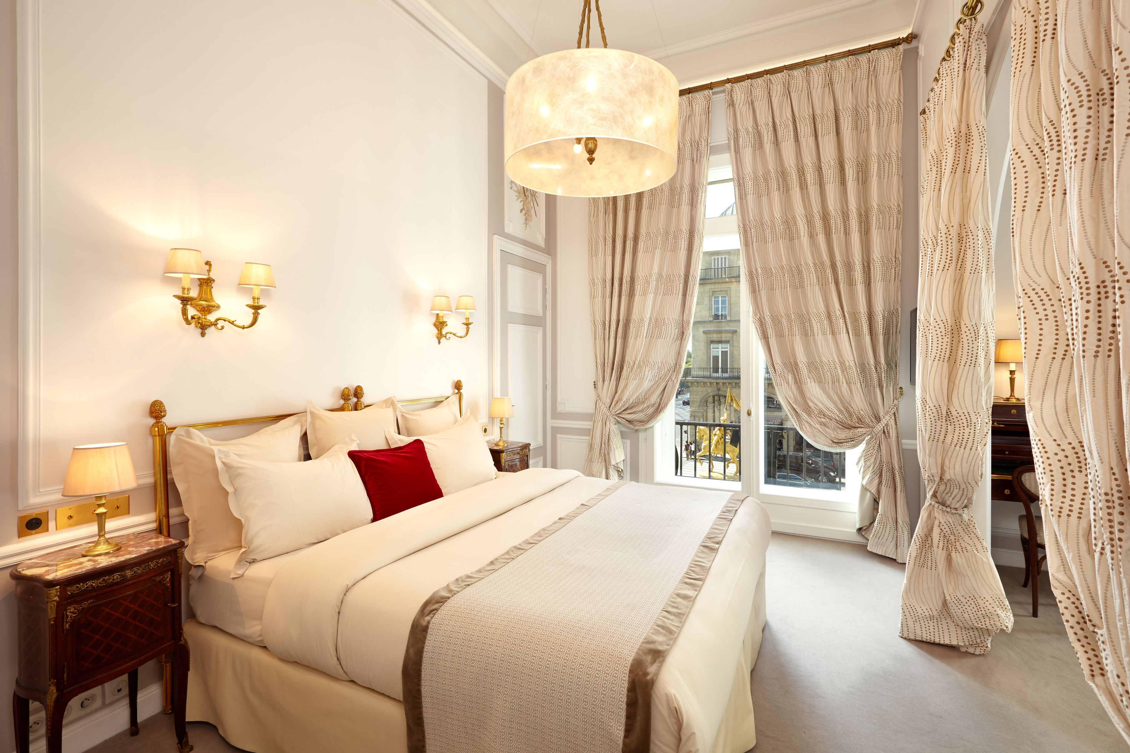 A spacious bedroom with a large bed, a chandelier, and a view of the city through the window.