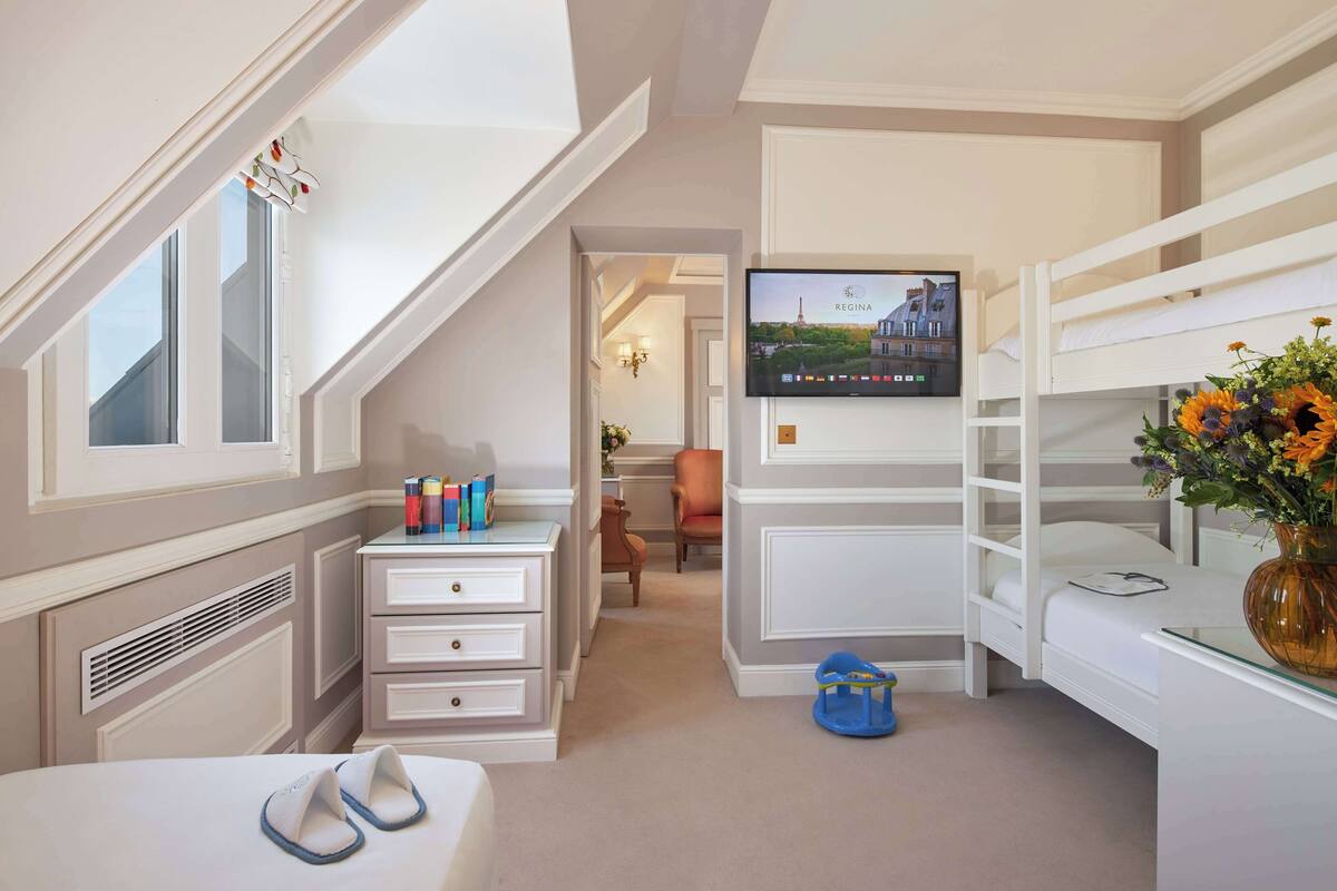 A hotel room with a bunk bed, a desk with a vase of flowers, a television mounted on the wall, and a small playhouse.
