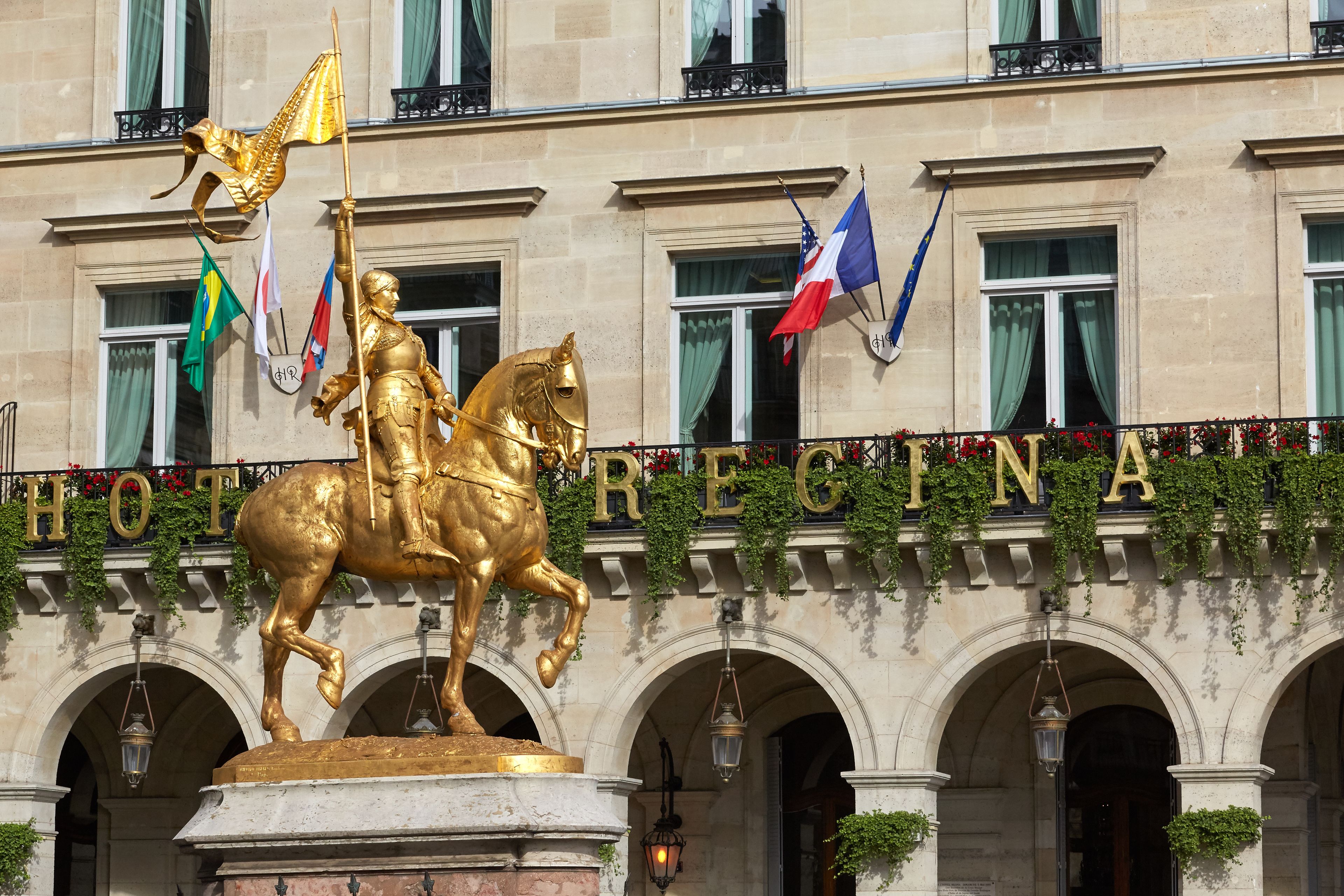 A golden statue of a figure on horseback, flags, and the word "HOTEL REGINA" on a building facade.