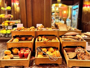 Wooden display cases filled with various baked goods like croissants, muffins, and bread, arranged on a marble countertop. - Hotel Regina Louvre (Paris)