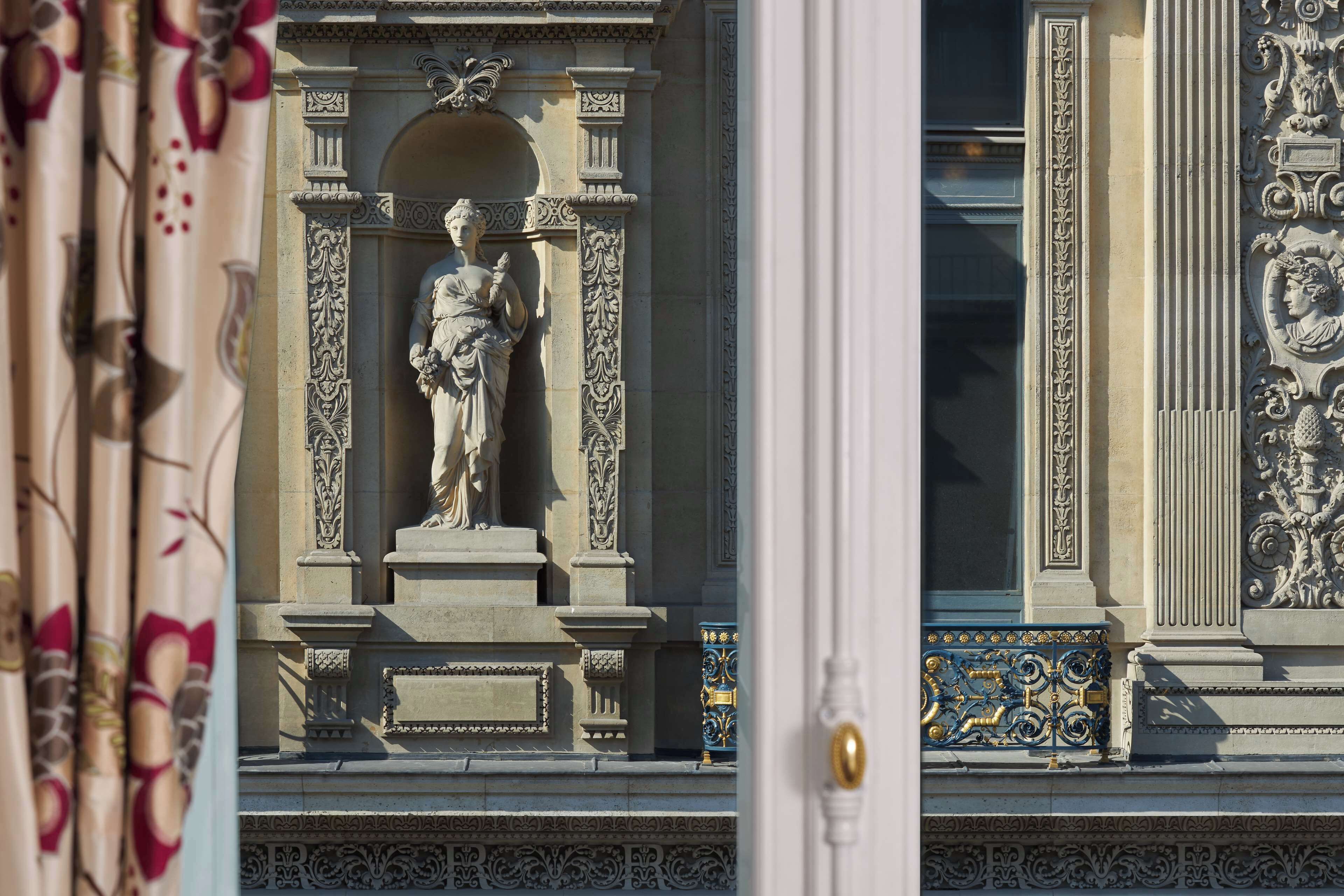 Una estatua clásica en un entorno arquitectónico ornamentado, con detallados relieves y una barandilla de metal decorativa.