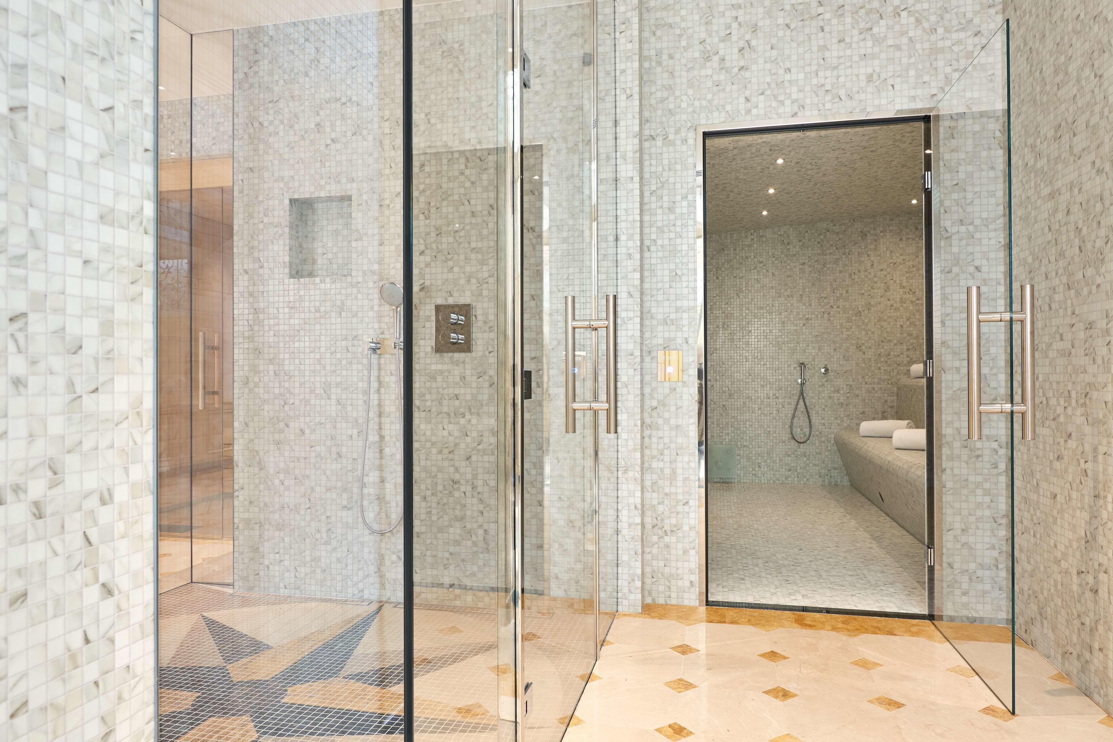 A modern bathroom with glass shower doors, a tiled floor, and a visible shower area.