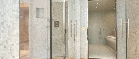 A modern bathroom with glass shower doors, a tiled floor, and a visible shower area.