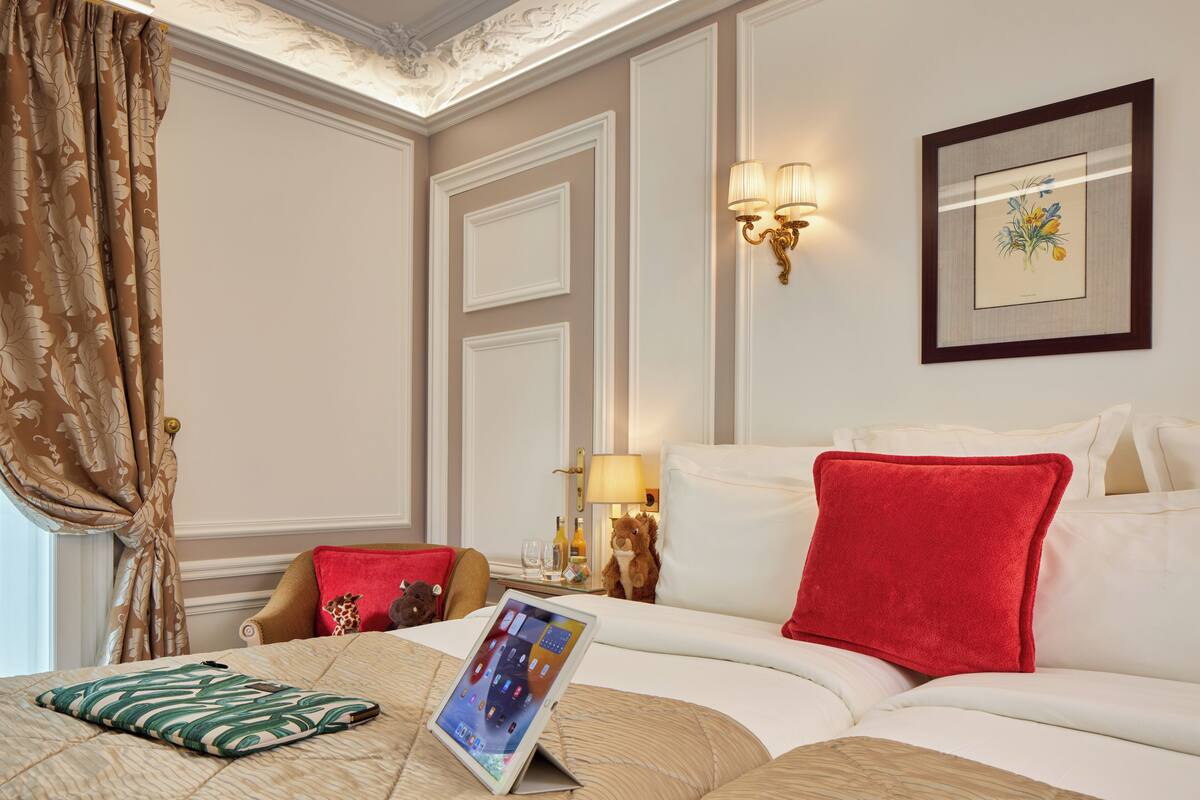 A hotel room with a bed, a bedside table with a lamp, a framed picture on the wall, and a window with curtains.