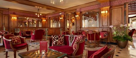 Un lobby lujoso con muebles ornamentales, una mesa de ajedrez y una planta grande en maceta.