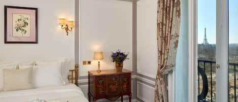 A hotel room with a bed, breakfast tray, a small table with a lamp, a decorative cabinet, and a view of the Eiffel Tower.