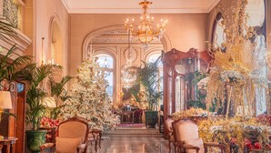 Un vestíbulo imponente con candelabros, muebles ornamentados y un árbol de Navidad.