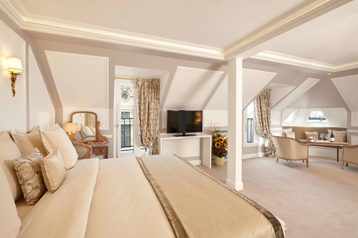 A spacious hotel room with a large bed, a desk, a television, and a seating area with a view of the city.