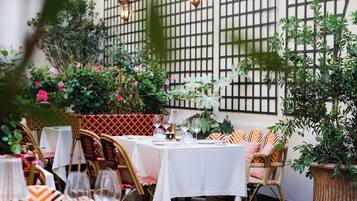 An outdoor dining area with tables set for two, surrounded by greenery and potted plants.