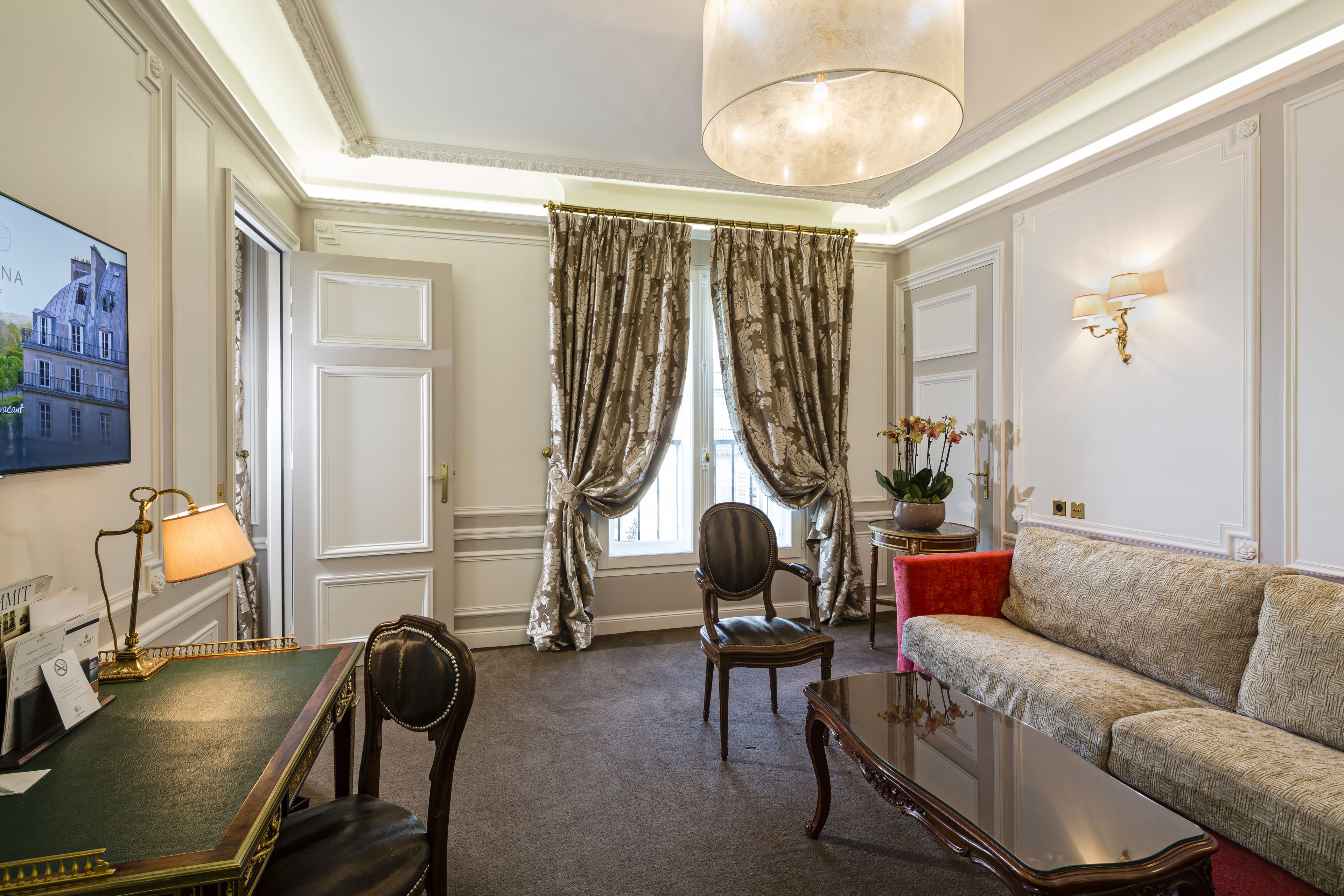 A room with a green desk, a leather chair, a wooden coffee table, a sofa, and a chandelier.