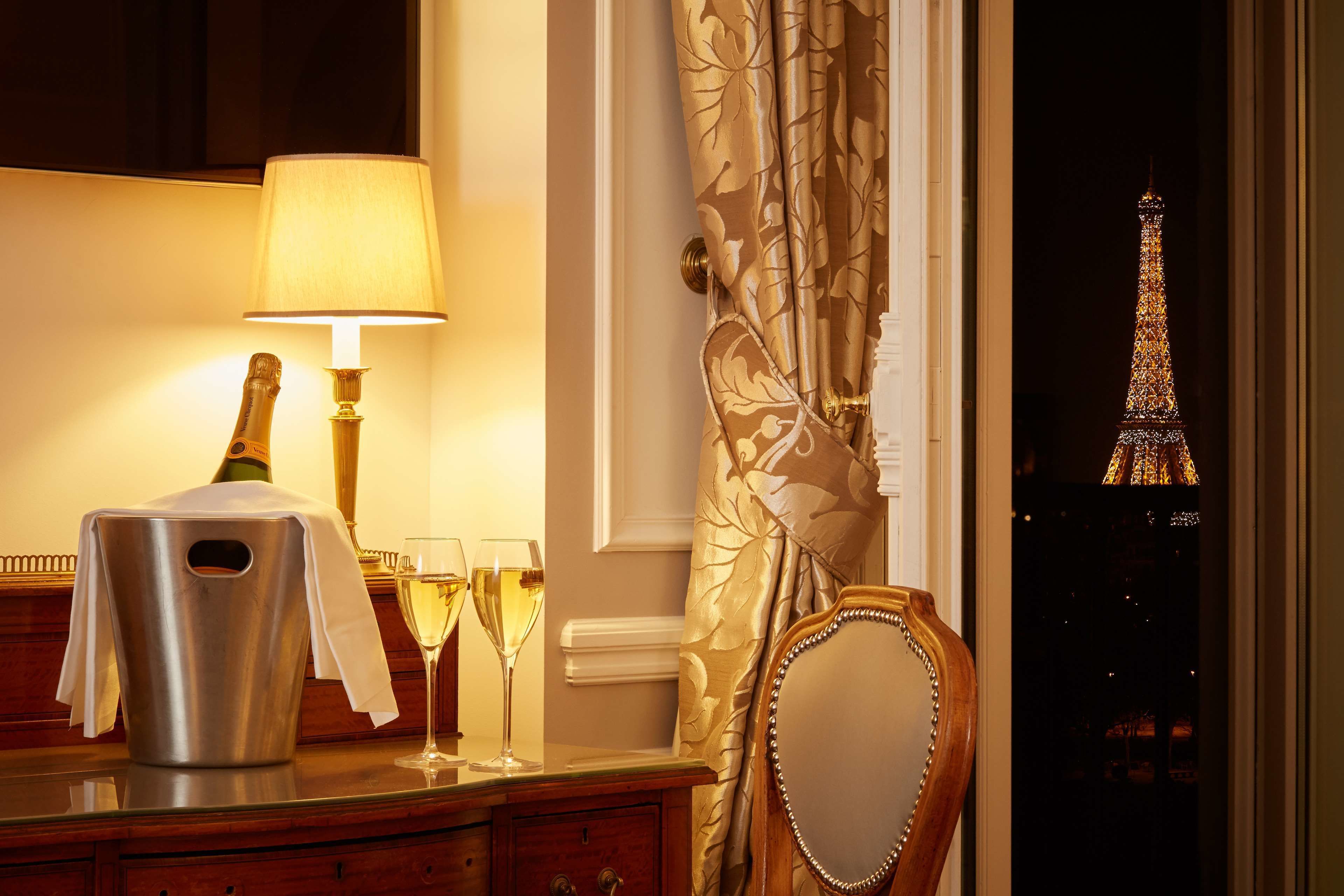 Una habitación con vistas a la Torre Eiffel, una botella de champán, una copa de champán, una lámpara y un espejo.