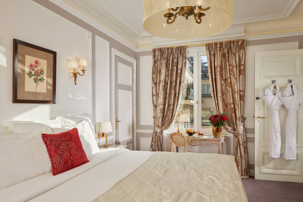 A well-appointed hotel room with a large bed, a sitting area with a table and chairs, and a view of the city through the window.