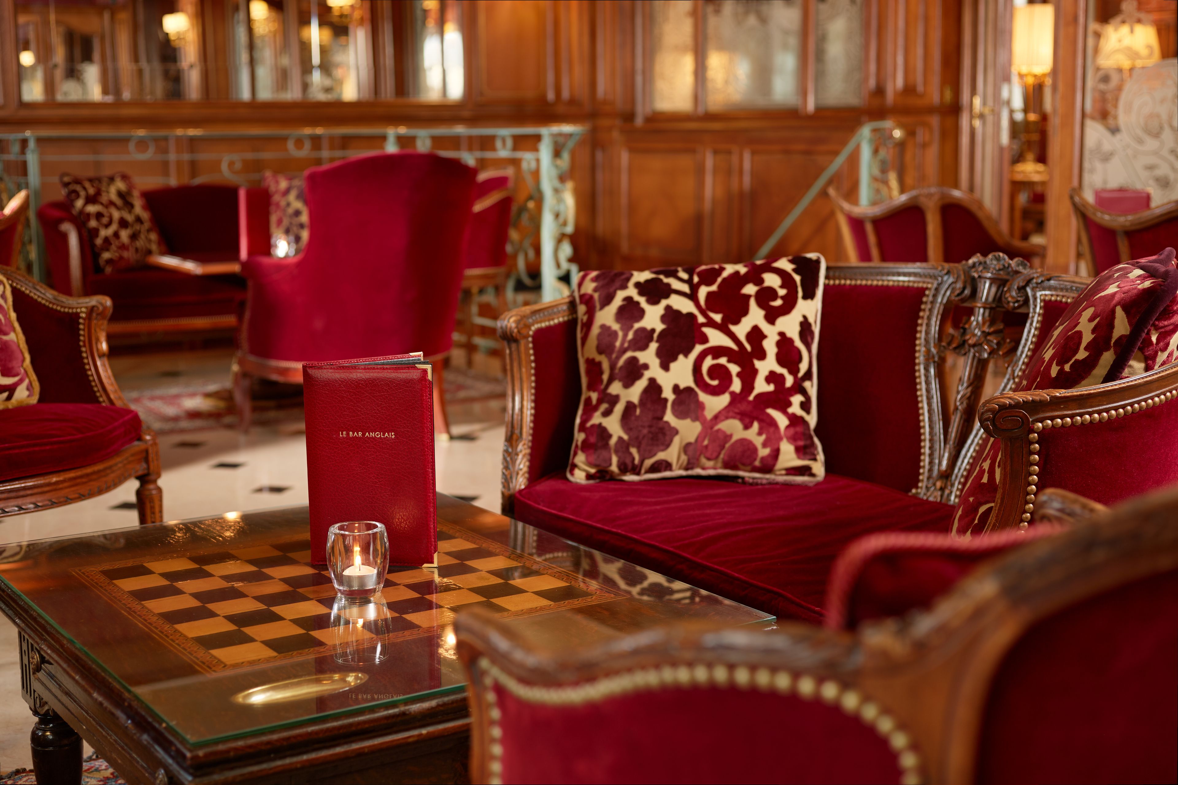 Una habitación lujosa con una mesa a cuadros, muebles tapizados en rojo y una vela pequeña.