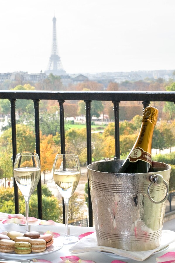 A balcony with a view of the Eiffel Tower, a champagne bottle, two glasses, and macarons on a table. - Hotel Regina Louvre (Paris)