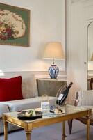 Ένα σαλόνι με έναν καναπέ, ένα τραπεζάκι σαλονιού από γυαλί, ένα βάζο, ένα φωτιστικό και έναν διακοσμητικό πίνακα με λουλούδια σε κορνίζα.