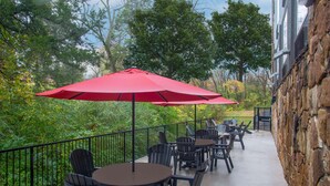 A patio with outdoor seating, a red umbrella, and a stone wall.