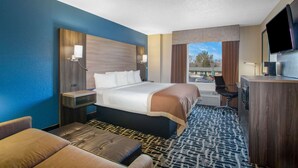 A hotel room with a large bed, a desk, a television, and a view of the outside.