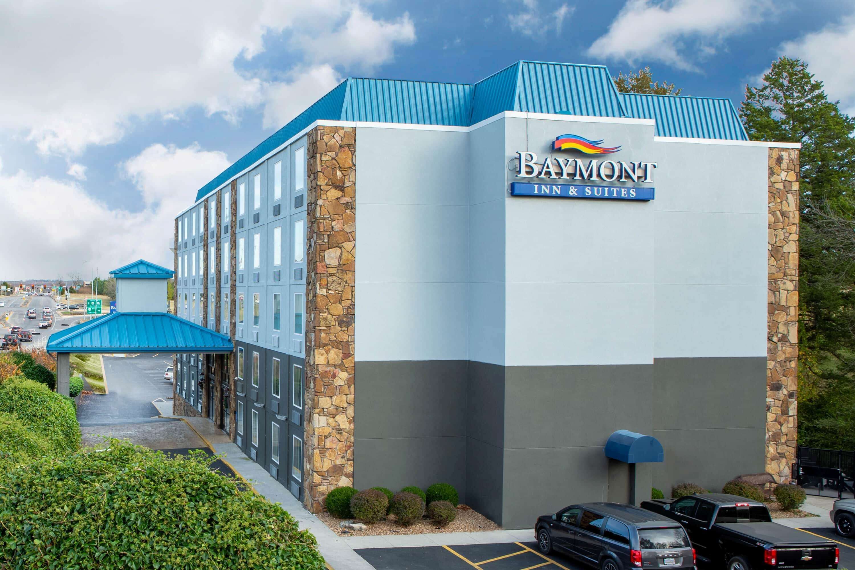 A Baymont Inn & Suites building with a blue roof, stone accents, and a parking lot with several cars.