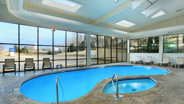 An indoor swimming pool with clear views of the outside, stone flooring, and several lounge chairs.