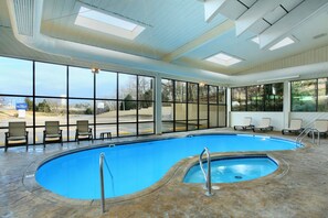 Una piscina interior con vistas despejadas al exterior, suelo de piedra y varias tumbonas.