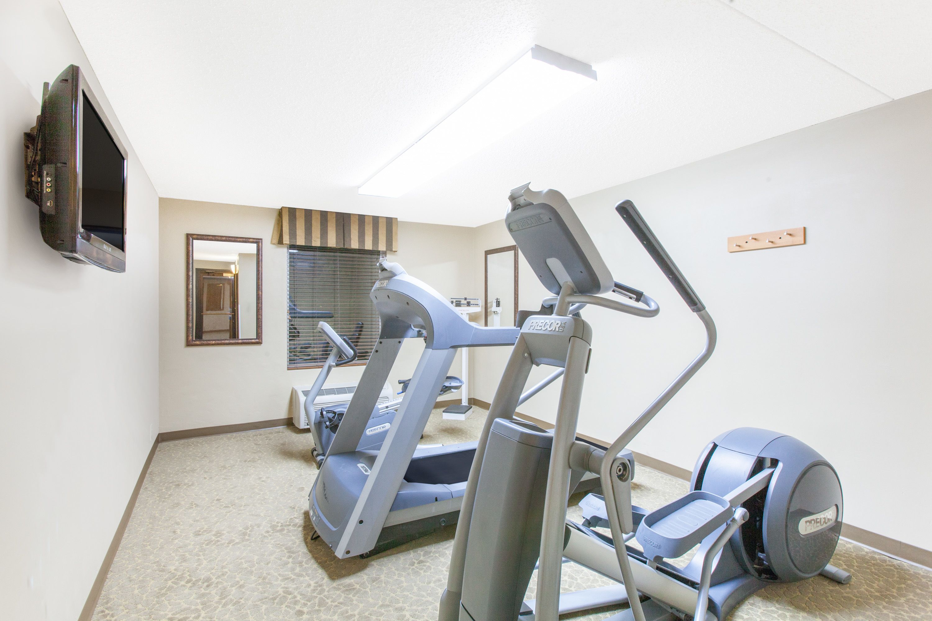 A fitness room with treadmills, an elliptical, and a TV mounted on the wall.