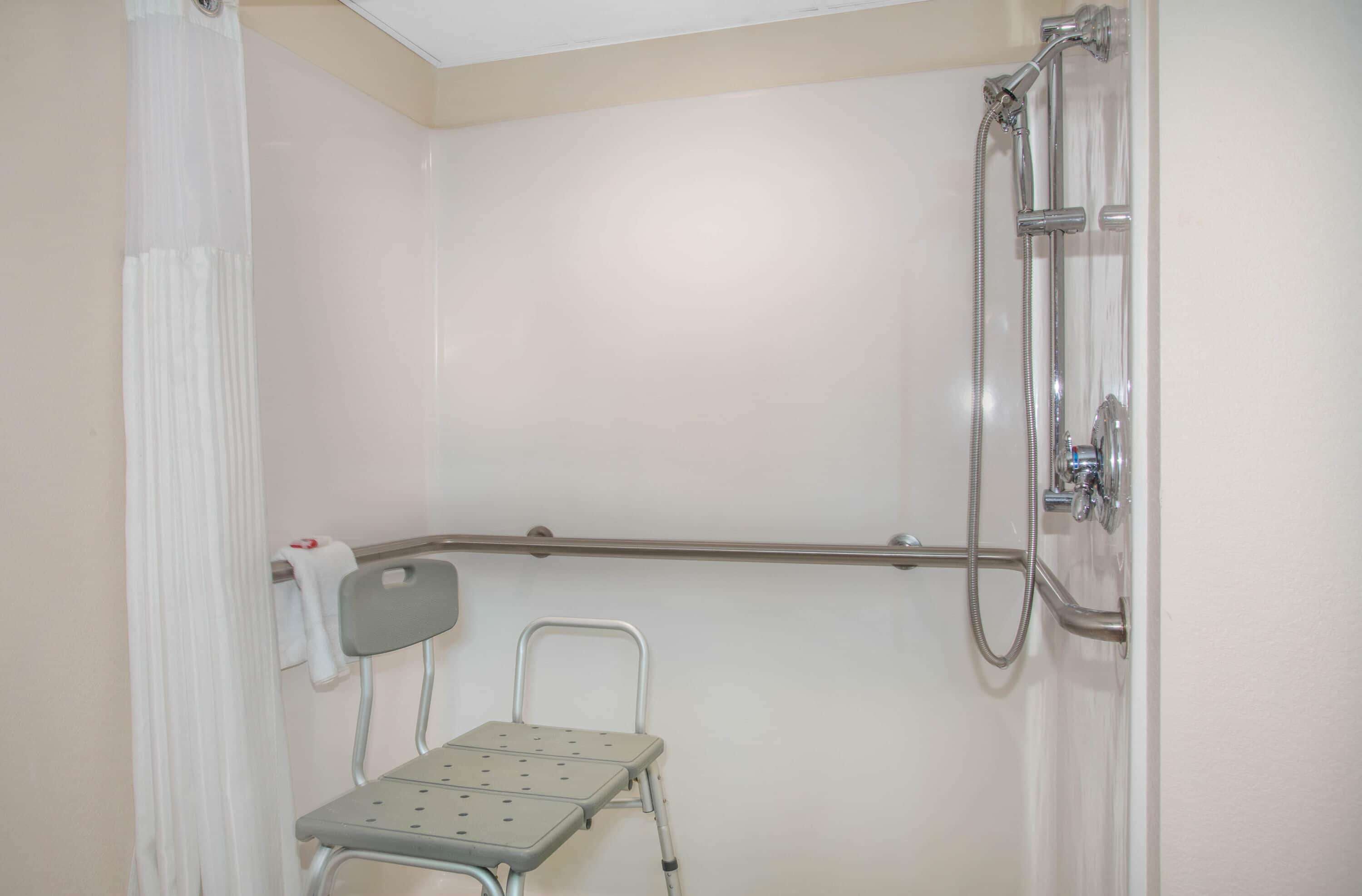 Un petit espace de douche fermé, équipé d’une barre d’appui, d’un marchepied et d’un porte-serviettes.