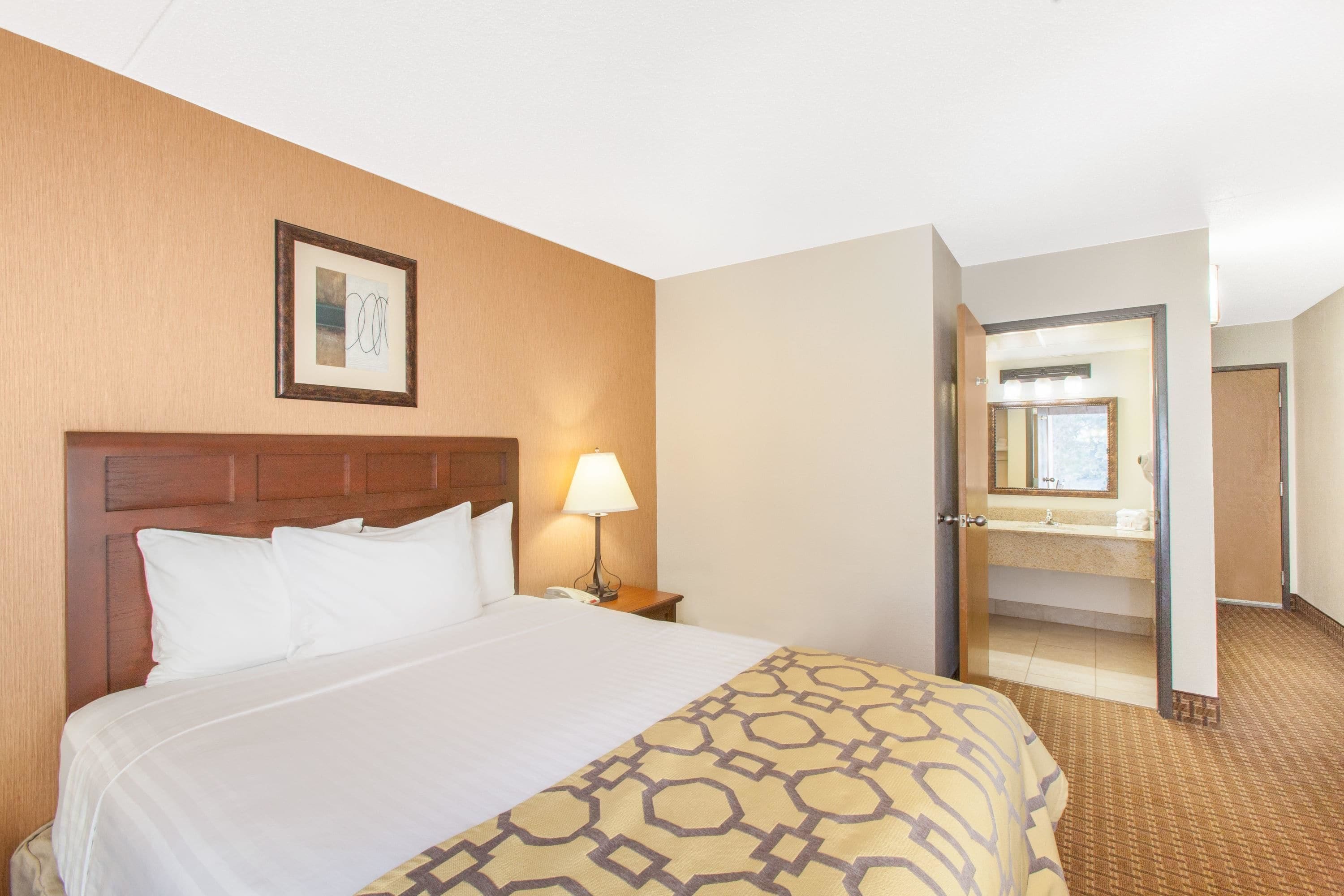 Habitación de hotel con una cama grande, una lámpara de noche, un cuadro en la pared y una puerta abierta que da a un baño.