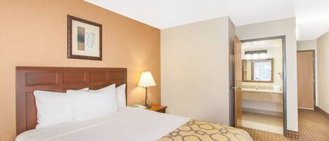 Habitación de hotel con una cama grande, una lámpara de noche, un cuadro en la pared y una puerta abierta que da a un baño.