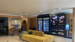 Un hall de hotel con un sofá amarillo, una computadora de escritorio y máquinas expendedoras.