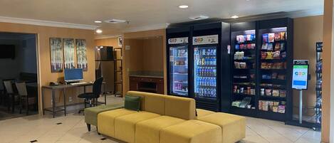 A hotel lobby with a yellow sofa, a desktop computer, and vending machines.