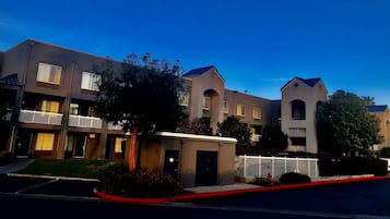 Una hilera de edificios modernos de varios pisos con balcones, un área de estacionamiento pequeña y una bordeadora roja.