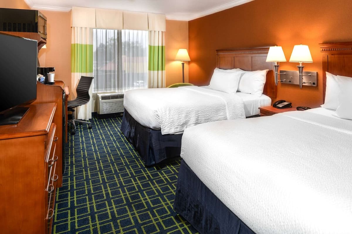 Une chambre d’hôtel avec deux lits, un bureau avec un ordinateur, une chaise, une télévision et une fenêtre avec des rideaux.
