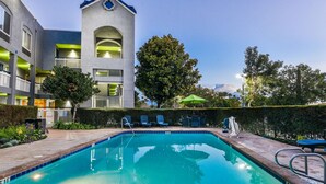 Una piscina con sillas de descanso y un edificio con balcones al fondo.