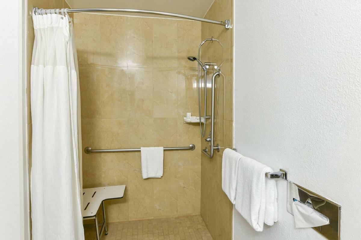 Un espace douche doté d’une porte en verre, d’une barre d’appui, d’un porte-serviettes et d’une serviette blanche accrochée au mur.