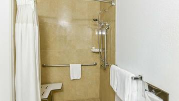 Zona de ducha con puerta de vidrio, barra de apoyo, toallero y una toalla blanca colgada en la pared.