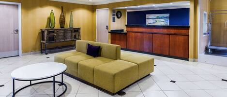 A lobby with a yellow sofa, a round table, a reception desk, and a clock on the wall.