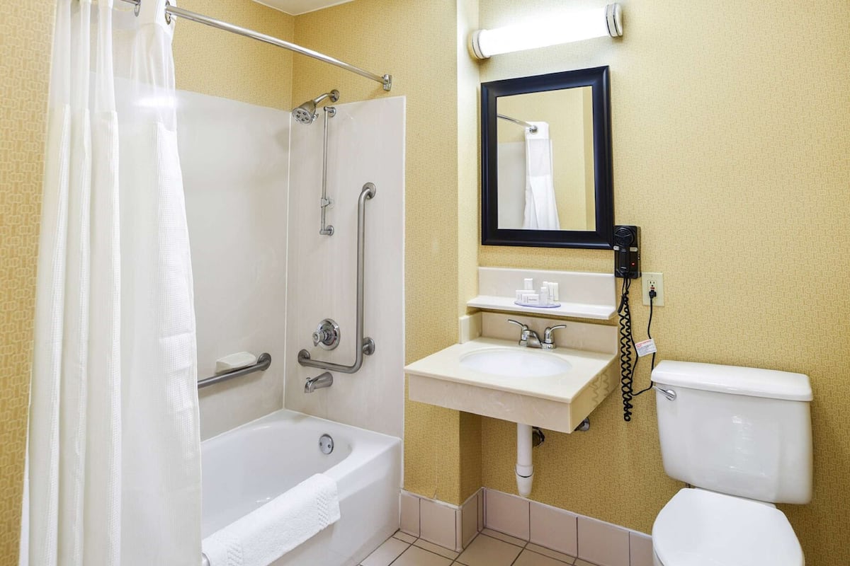 Une salle de bain équipée d’une baignoire, d’une douche avec des barres d’appui, d’un lavabo et de toilettes.