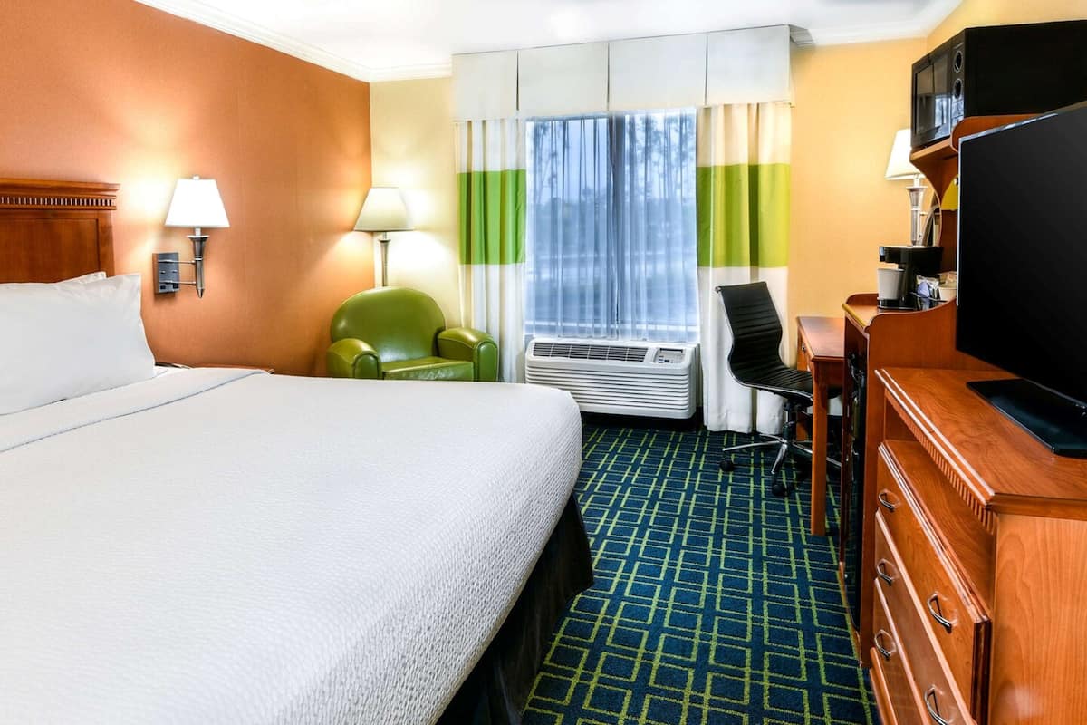 Une chambre d’hôtel avec un grand lit, un bureau avec une télévision, une chaise et un appareil de climatisation.