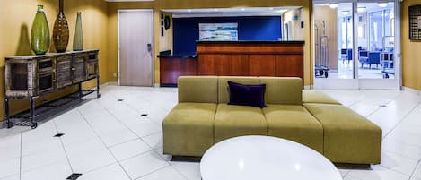 A lobby with a sofa, a round table, a reception desk, and a wall-mounted painting.