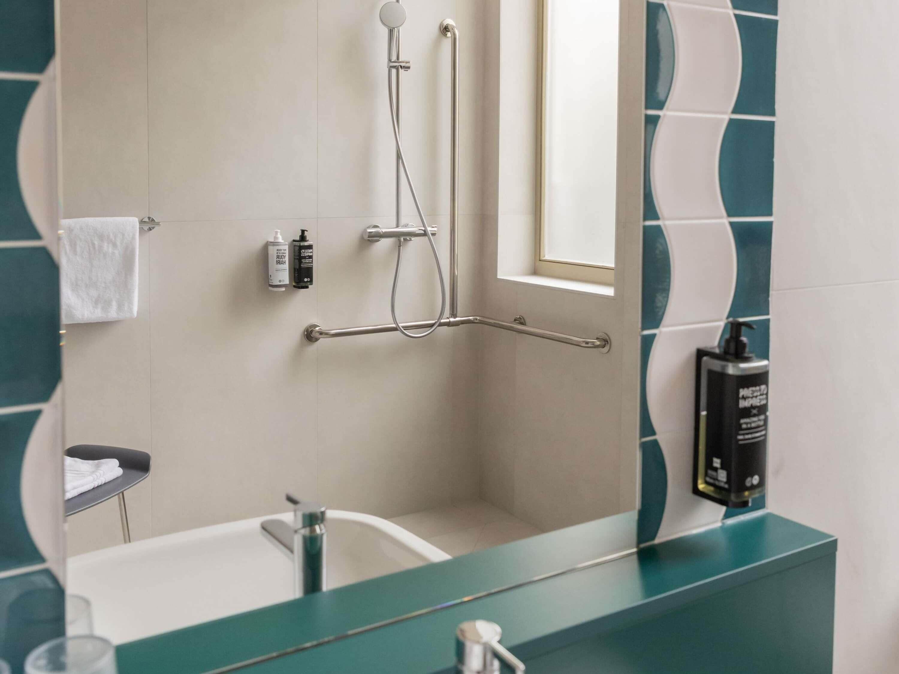 A modern bathroom with a bathtub, a shower with a handheld showerhead, a grab bar, and a window above the sink.